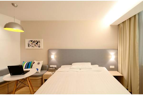 A well-lit bedroom with a large bed and a laptop on a table.